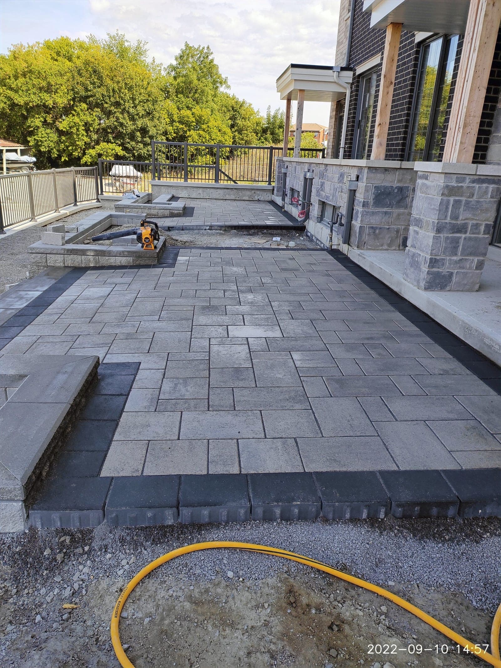 Grey interlock patio with charcoal border behind a stone home